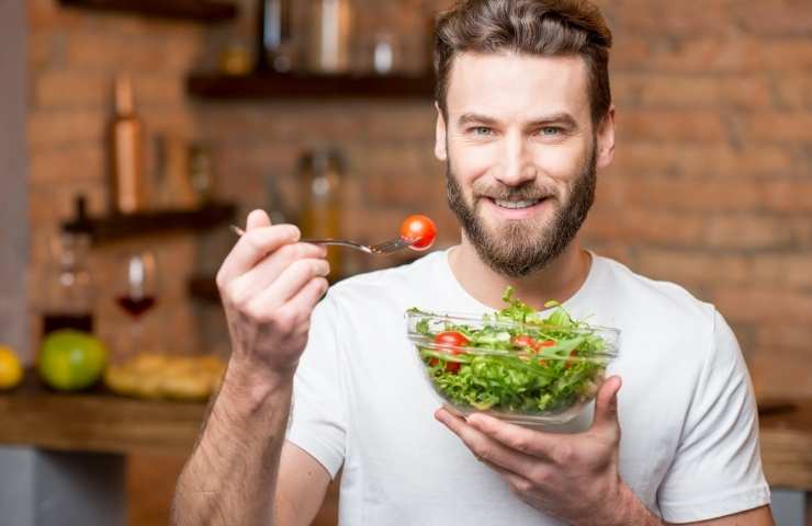 uomo che mangia insalata di pomodori