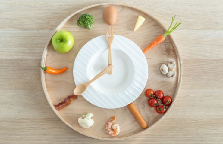 Un orologio formato da piatto, posate e alimenti sani